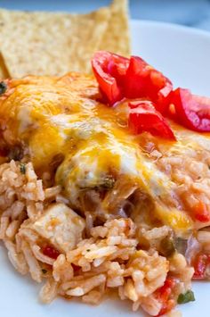 a white plate topped with rice covered in cheese and veggies next to tortilla chips