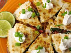 an orange plate topped with quesadillas covered in sour cream and green onions