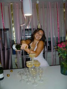 a woman is pouring champagne into glasses at a table with pink and gold streamers