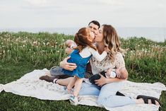 a man and woman kissing while sitting on a blanket in the grass with their child