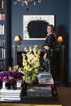 a woman standing in front of a table with flowers on it and books stacked on top