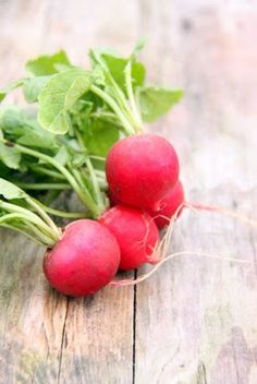 three radishes with green leaves on a wooden surface