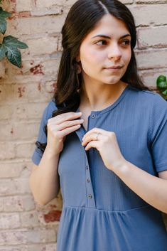 a woman is standing in front of a brick wall and adjusting her shirt with one hand