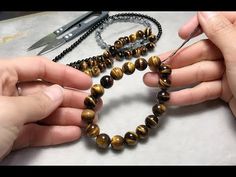 two hands holding beads and scissors on a table