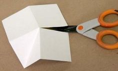 scissors cutting out paper on top of a piece of white paper with an orange handle