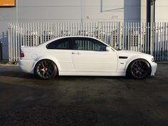 a white car is parked in front of a building with a fence and gate behind it