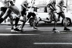 black and white photograph of people running in the street with cars passing by behind them