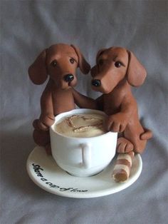 two brown dogs sitting on top of a white plate next to a cup of coffee