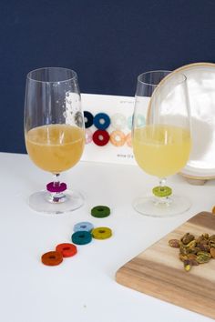 two wine glasses filled with liquid next to buttons on a cutting board and corks