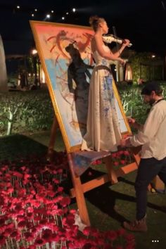 a man and woman standing next to an easel with paintings on it at night