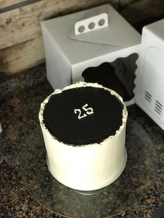 a white cake with black frosting and the number twenty five on it sitting on a counter