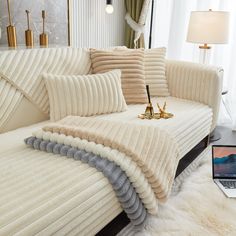 a laptop computer sitting on top of a white couch next to pillows and rugs