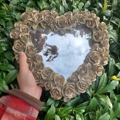 a heart shaped mirror in the middle of some green plants and leaves with a hand holding it