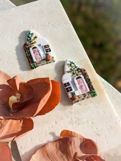 three small houses are sitting on a table with flowers in the foreground and one has a pink flower