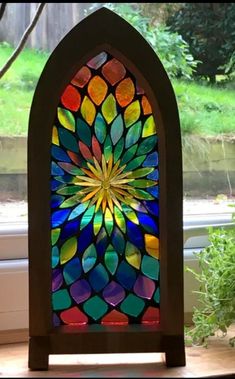 a colorful stained glass window sitting on top of a wooden table next to a potted plant