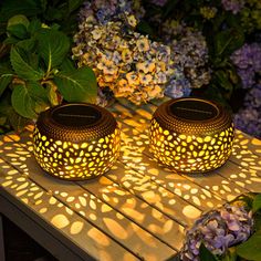 two lit candles sitting on top of a wooden table next to purple and white flowers