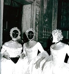 three women in white dresses with masks on their faces sitting next to each other and looking at the camera