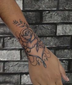 a person with a rose tattoo on their arm and hand, next to a brick wall