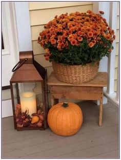 a basket full of orange flowers next to a lantern and pumpkin on the front porch