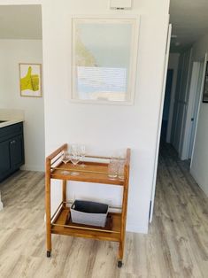 a kitchen with white walls and wood flooring has a bar cart in the middle