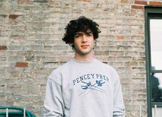 a young man standing in front of a brick wall wearing a sweatshirt that says penncy prep