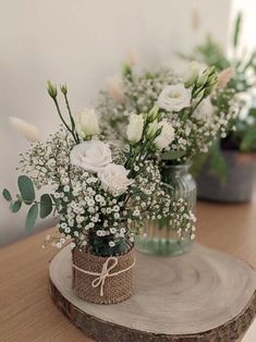 two vases filled with white flowers sitting on top of a wooden table next to each other