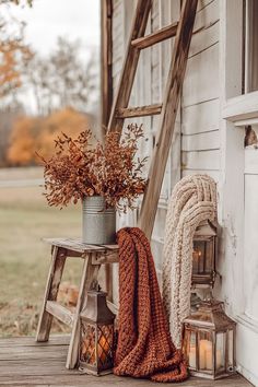 Cozy fall decor with a rustic ladder, autumn flowers in a tin vase, cozy blankets, and lanterns on a porch. Perfect fall decorating ideas for the home.