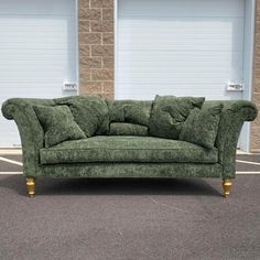 a green couch sitting on top of a parking lot next to two garage doors with roller doors in the background