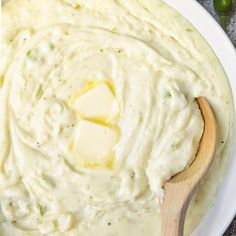 a bowl filled with mashed potatoes on top of a table next to a wooden spoon