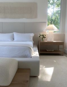 a white bed sitting next to a window with a lamp on top of the headboard