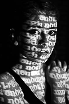 a woman with words all over her body and face in black and white, looking at the camera