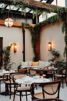 an outdoor restaurant with tables and chairs covered in greenery, hanging lights and potted plants