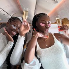 two women with face paint on their faces holding champagne flutes in the air while sitting next to each other