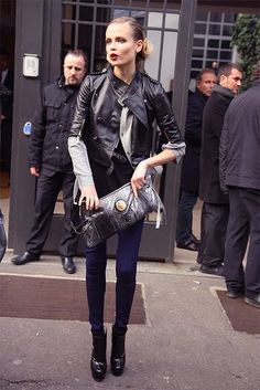 a woman is walking down the street carrying a purse and wearing all black, with other people in the background