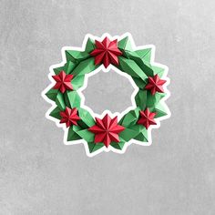 an origami christmas wreath with red and green stars on the top, hanging from a gray wall