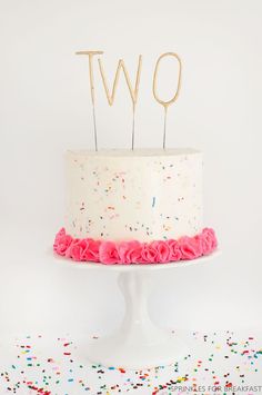 a two tiered cake with sprinkles on it and the number two spelled out