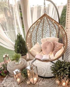 a hanging chair with pillows and candles on the ground next to plants, lanterns and potted plants