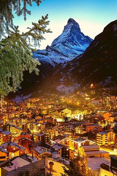 the city is lit up at night with mountains in the background