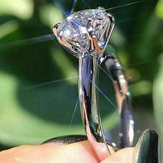 a close up of a person's hand holding a ring with a diamond on it