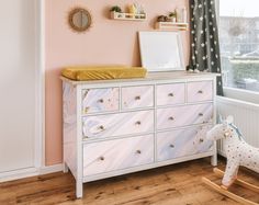 a baby's room with pink walls and white furniture, including a rocking horse