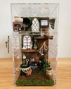 a doll house in a clear plastic case on a wooden table with lots of decorations