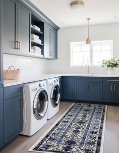 a washer and dryer in a kitchen with blue cabinetry, white counter tops, and wooden floors