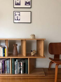 a wooden shelf with books and vases on it in front of two framed pictures