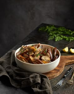 a white bowl filled with clams on top of a wooden cutting board next to lemon wedges