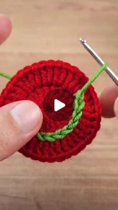 someone is crocheting a red flower with green yarn