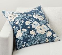 a white couch with a blue floral pillow on it's back and arm rest