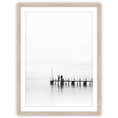 a black and white photo of two people standing on a pier in the middle of water