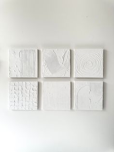 four pieces of white art hanging on a wall next to a vase with flowers in it