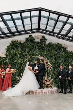 a bride and groom standing in front of an arch with greenery