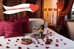 two glasses of champagne on a tray with rose petals in front of a bed decorated with roses